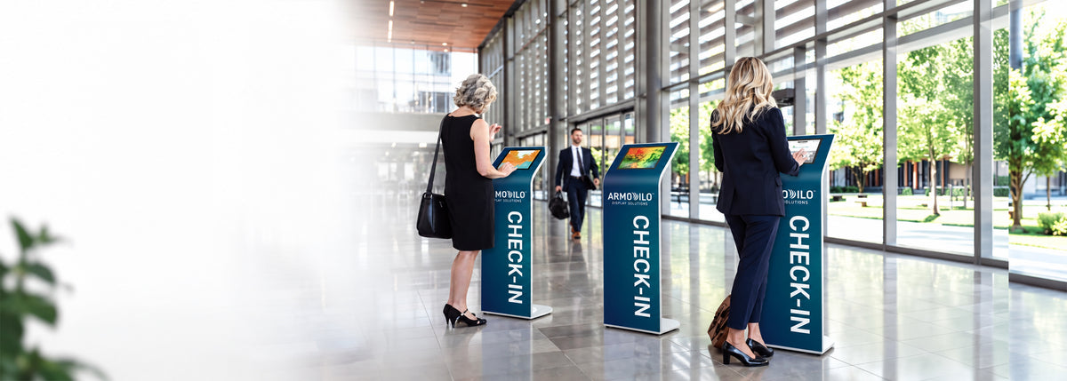 Visitors using three branded Armodilo check-in kiosks in a bright office building lobby