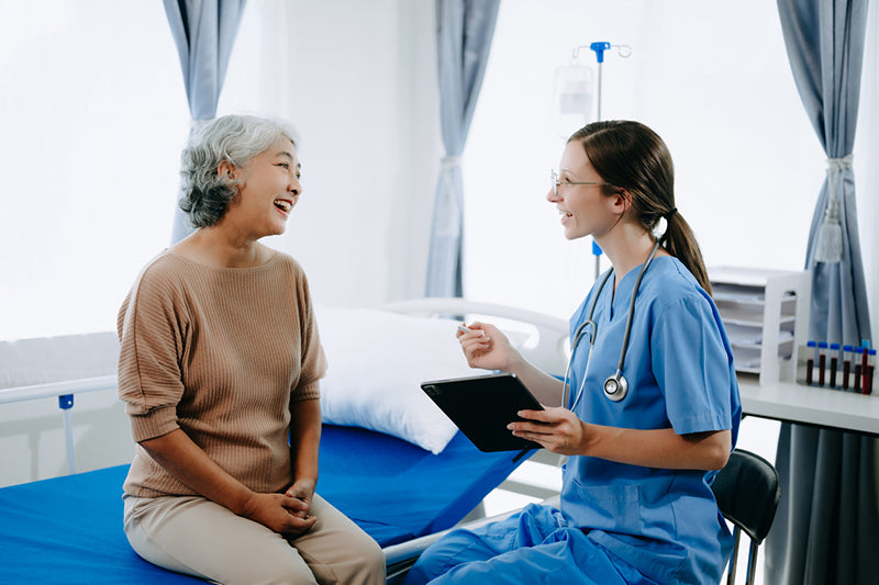 Nurse with a tablet talking to an elderly patient in a hospital room.