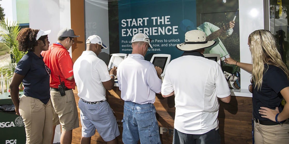 Attendees using Armodilo tablet kiosks displaying a "Start the Experience" screen at the US Open American Express Fan Experience