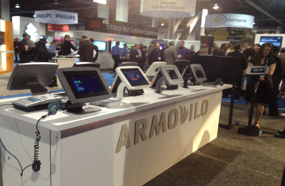 Armodilo booth at a trade show displaying tablet stands and enclosures with a card reader